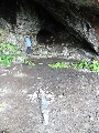 
	  The cross at the front of the cave.  On the right (centre) is
	  the font, surrounded by bracken, which collects water
	  	dripping from the outside of the cave.
	